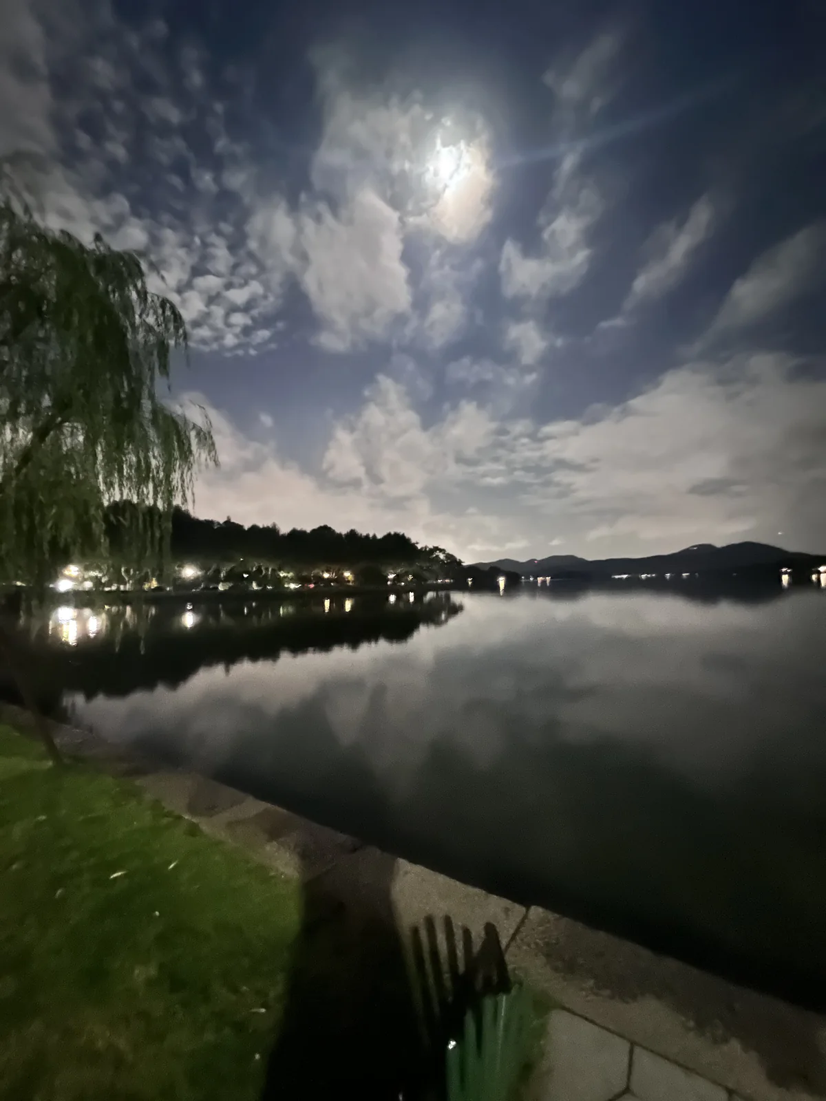 月光穿过云层照亮湖面,岸边树木与远山倒映在水中