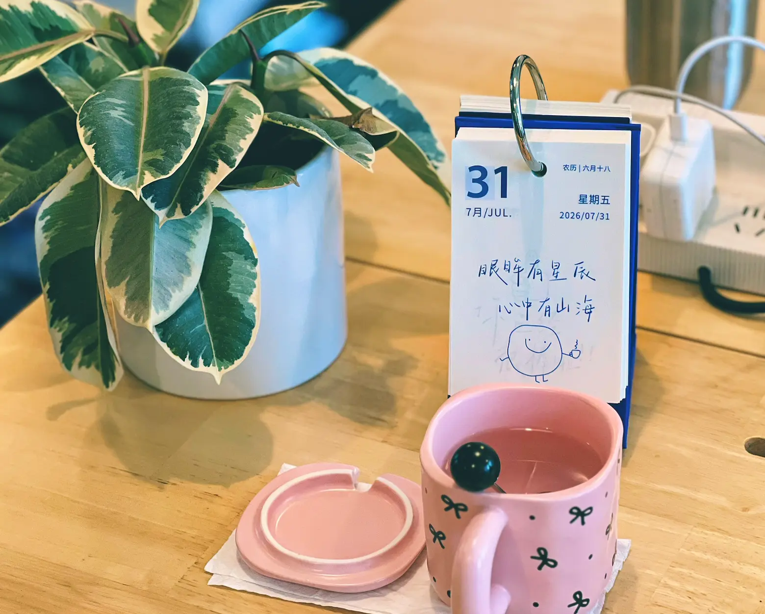 事橙办公室桌面上的日历、绿植与粉色水杯